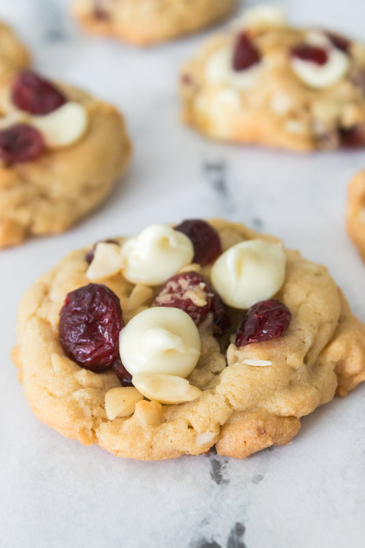 close up vertical shot of white chocolate cranberry cookies topped with white chocolate chips, dried cranberries and macadamia nuts