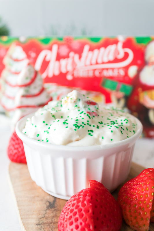head on vertical shot of little debbie christmas tree cake dip in white serving dish with strawberries