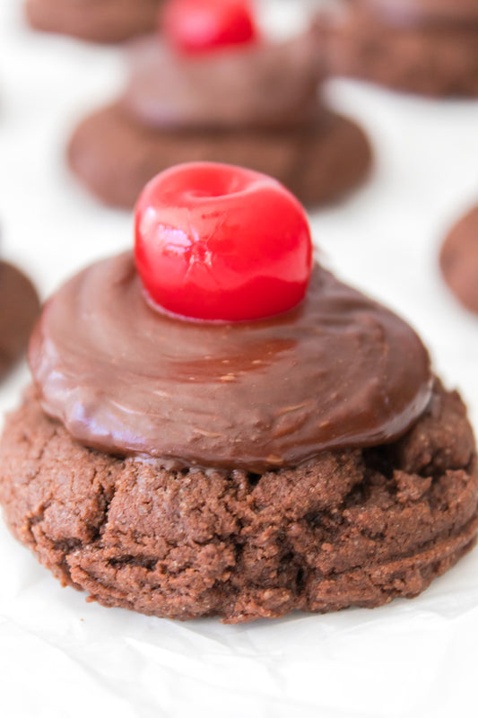 close up vertical head on shot of chocolate cherry cookies with chocolate icing topped with a maraschino cherry