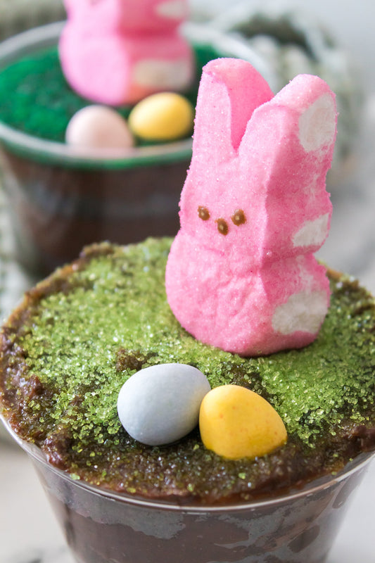 close up vertical shot of green sugar sprinkles and cadbury eggs with pink easter bunny peeps on dirt cup