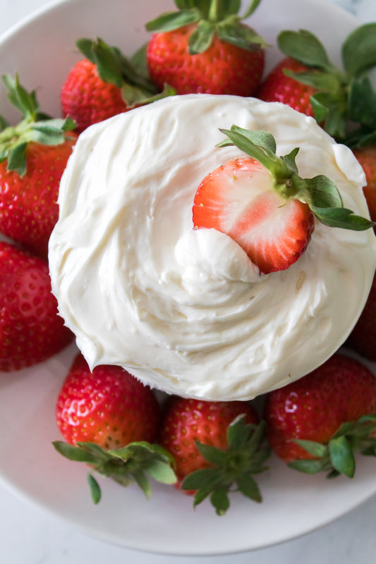 overhead shot of strawberries on white plate with bowl of fruit dip with a strawberry dipped in that has been sliced in half