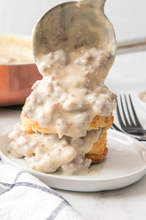 laddle pouring sausage gravy over biscuits