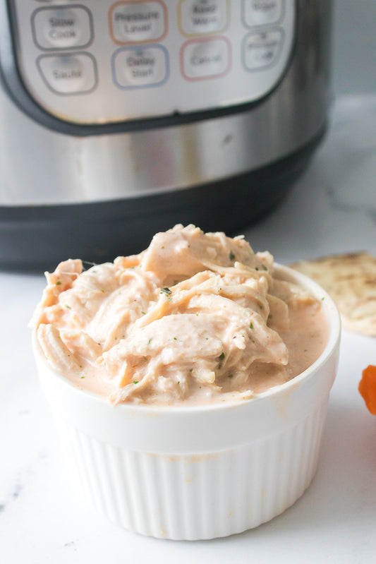 close up shot of buffalo chicken dip in white serving bowl with instant pot in background