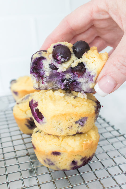 hand placing a keto blueberry muffin on top of another muffin with bite taken out