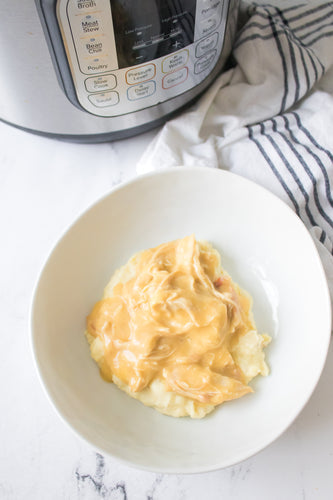 close up vertical shot of chicken gravy served over mashed potatoes in white bowl with instant pot in background