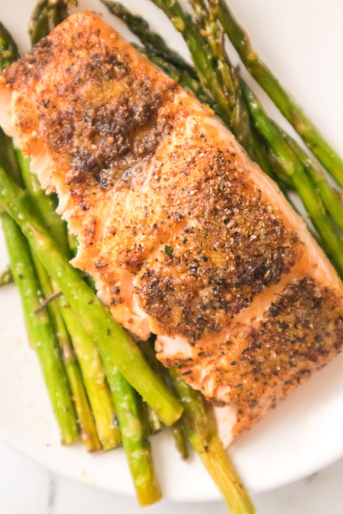 asparagus topped with air fryer salmon served on white plate