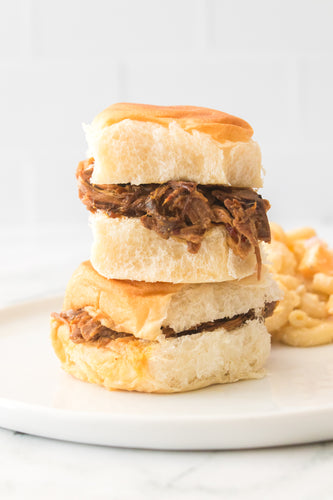 two pulled pork sliders stacked on top of one another on white plate