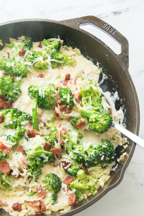 bacon and broccoli cooked in cast iron skillet in creamy garlic sauce topped with shredded mozzarella cheese