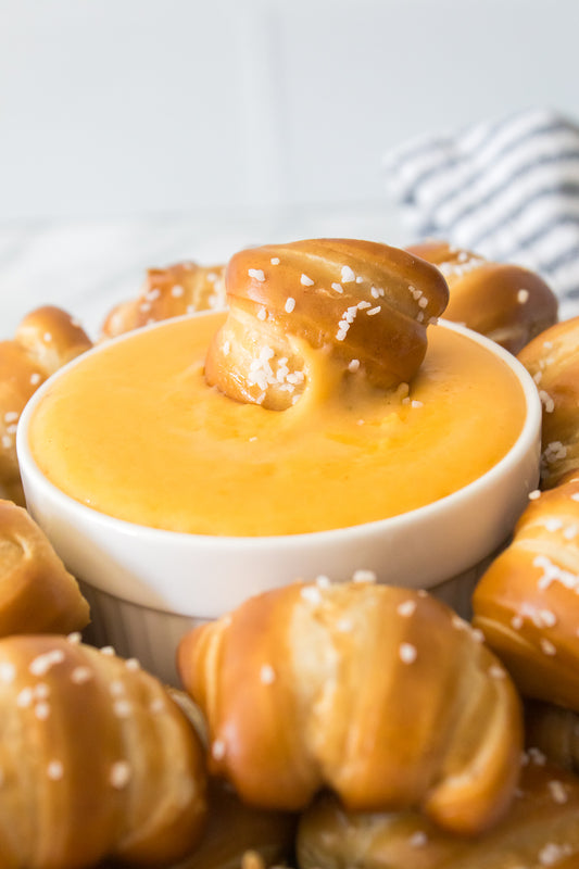 Close up vertical shot of a soft pretzel sitting in beer cheese on a serving platter surrounded by bite sized soft pretzels