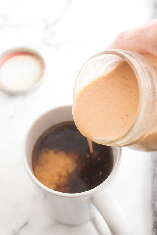 hand pouring mason jar with homemade pumpkin spice coffee creamer into mug with coffee