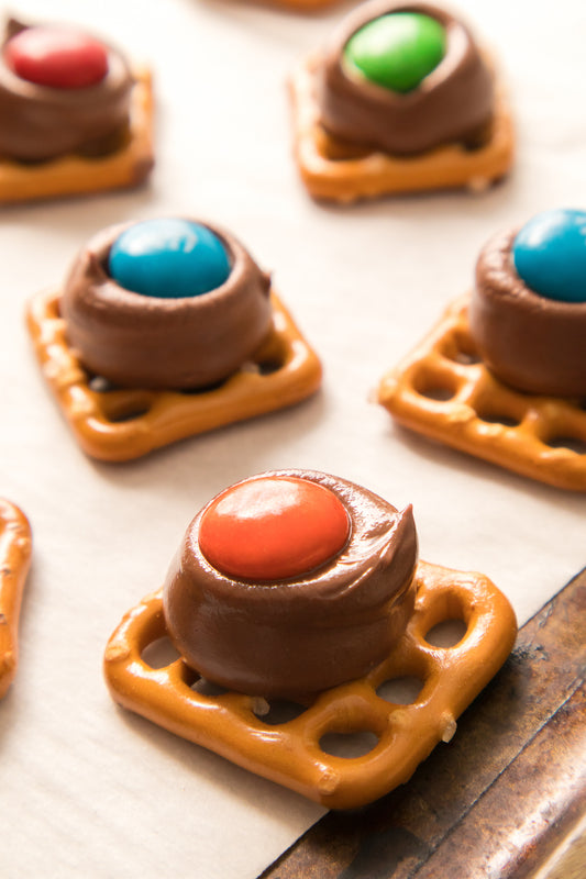 close up vertical shot of Hershey Kiss pretzels on baking sheet with parchment paper