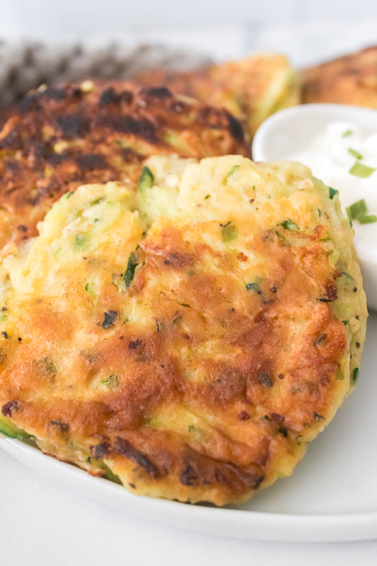 close up vertical shot of zucchini fritter on white plate served with sour cream for dipping