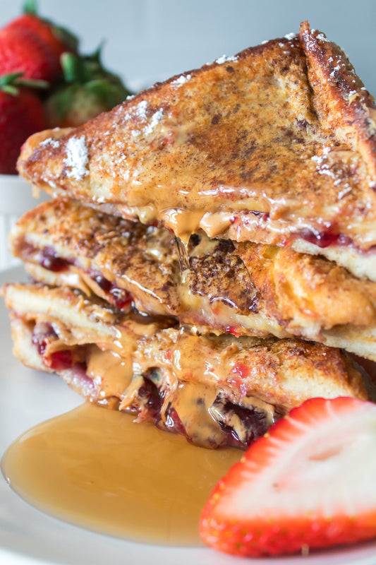 close up vertical shot of peanut butter and jelly french toast cut in half, stacked on top of one another with syrup drizzling down dusted with powdered sugar