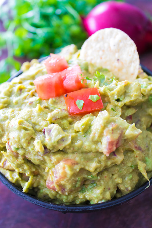 close up vertical shot of guacamole in guacamole serving dish topped with diced tomatoes and chopped cilantro