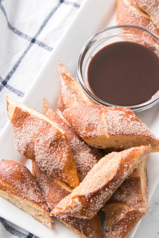 overhead shot of pieces of soft pretzels coated in cinnamon sugar mixture with bowl of chocolate syrup