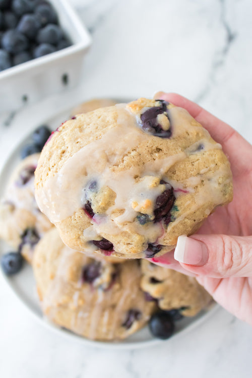 hand holding blueberry biscuit with glaze over plate over biscuits