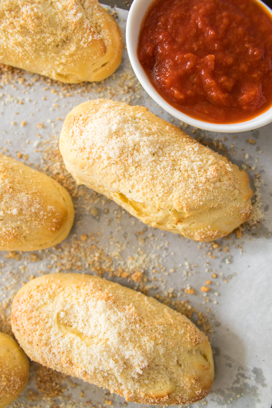 overhead shot of biscuit breadsticks on baking sheet with bowl of marinara sauce